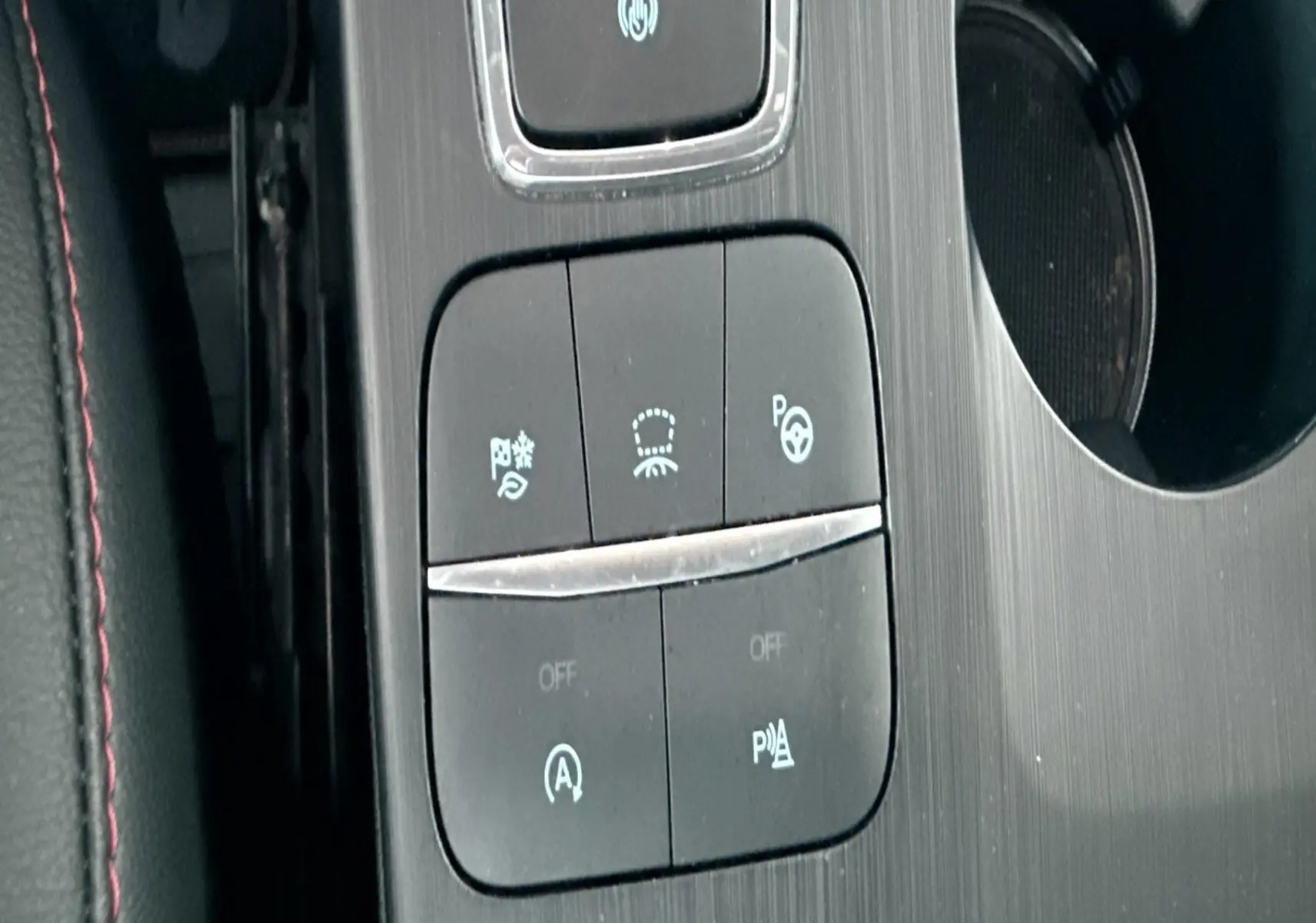 Gros plan sur la console centrale noire du Ford Kuga bleu azur 2023, avec boutons de contrôle et surpiqûres rouges visibles.