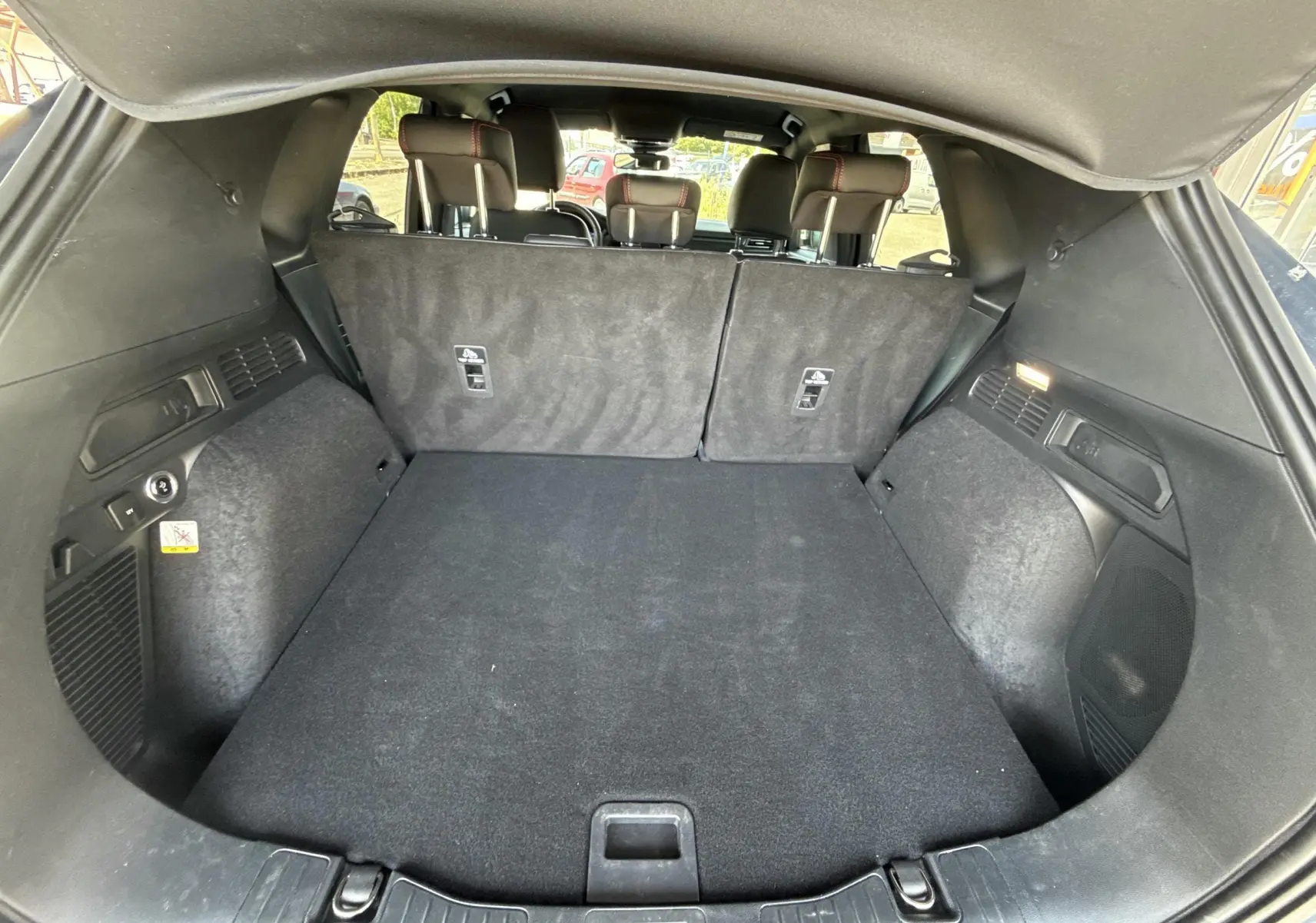 Coffre spacieux ouvert du Ford Kuga bleu azur 2023, avec banquette arrière rabattue et habillage intérieur noir.