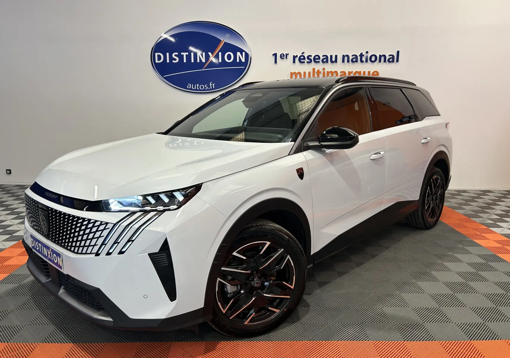 Peugeot 5008 Hybrid blanc vue 3/4 avant droit, avec jantes noires et toit noir brillant en intérieur showroom.