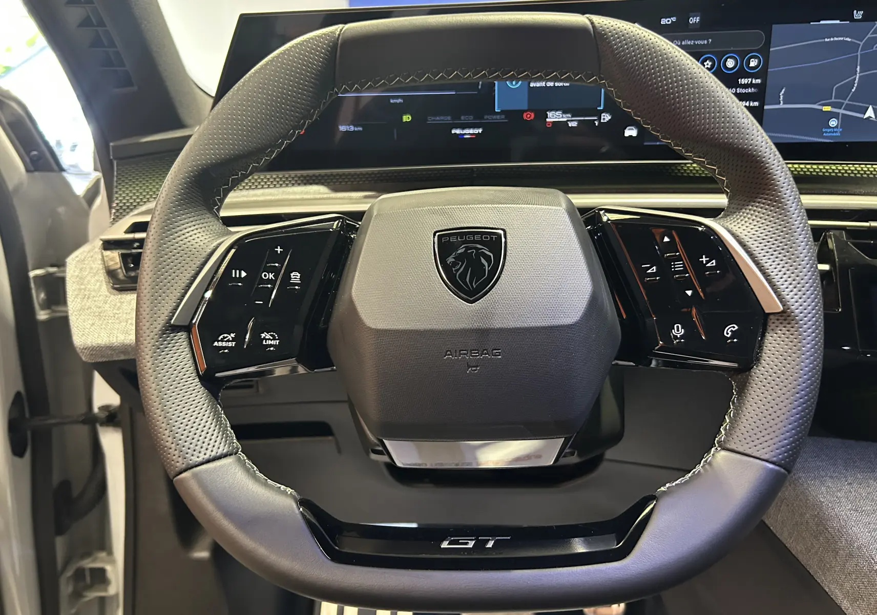 Vue rapprochée du volant cuir perforé du Peugeot 5008 Hybrid 2025 avec logo et commandes intégrées.