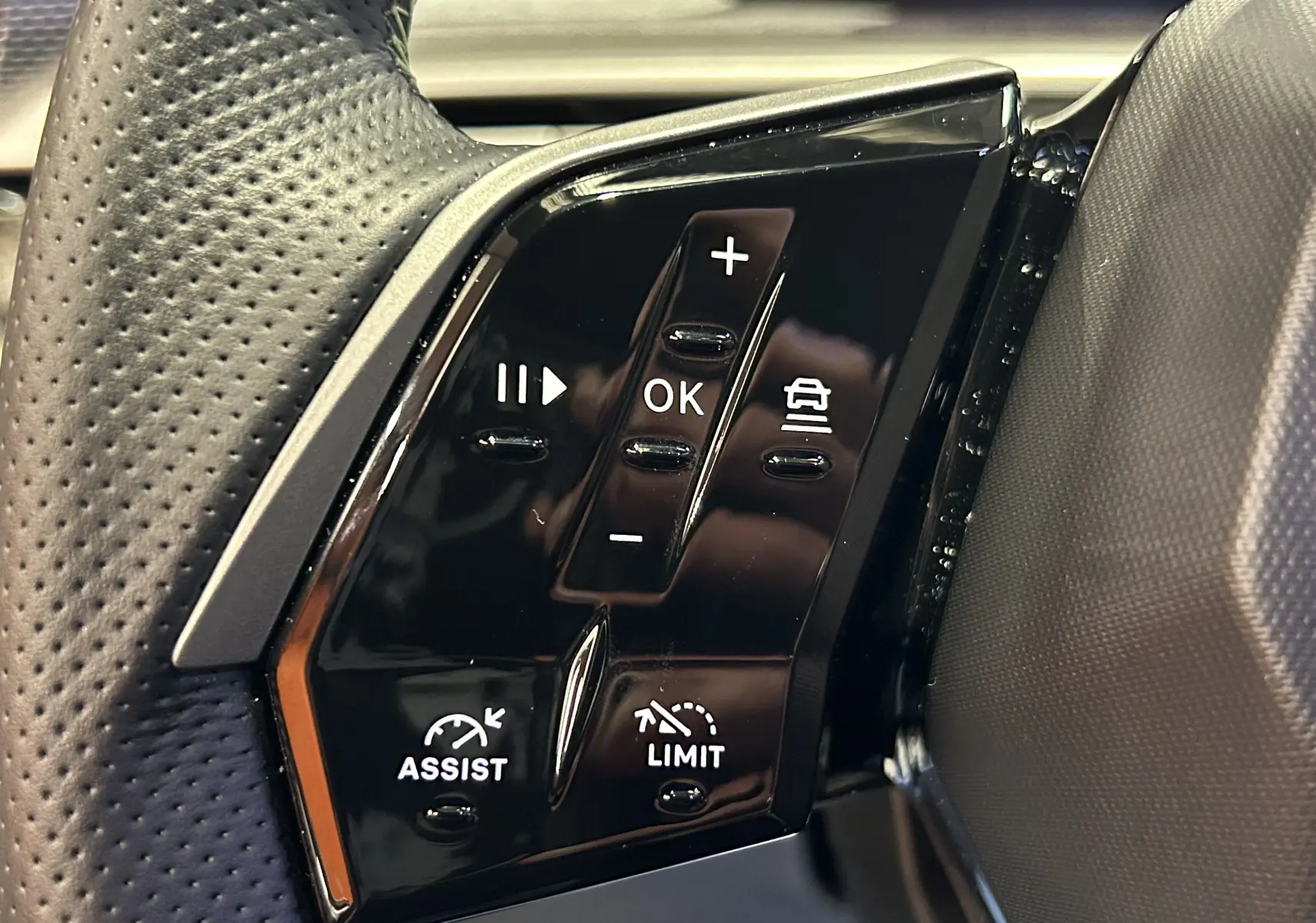 Gros plan sur les commandes noires du volant côté gauche du Peugeot 5008 Hybrid blanc, avec boutons d'assistance et limitation.