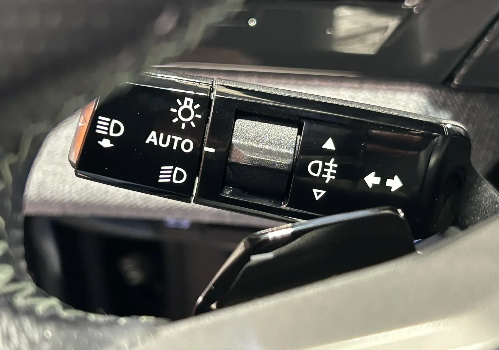 Gros plan sur la commande des phares et clignotants du Peugeot 5008 Hybrid blanc, côté gauche du volant.