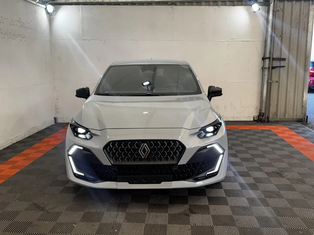 Renault Clio Techno TCe 115 gris clair vue de face, phares LED allumés et calandre distinctive en intérieur.