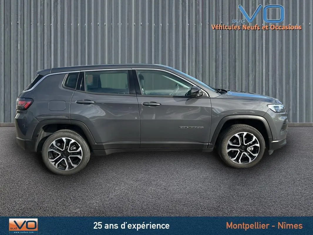 Profil côté gauche du Jeep Compass gris 2024 garé devant un mur métallique, roues alliage visibles.