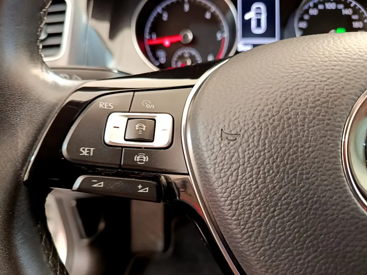 Gros plan sur la partie gauche du volant cuir de la Volkswagen Golf gris clair, avec commandes de régulateur adaptatif visibles.