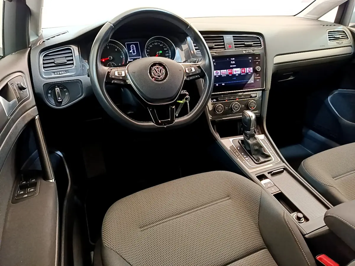 Intérieur de Volkswagen Golf gris clair 2019, vue du poste de conduite avec volant cuir et écran tactile central.