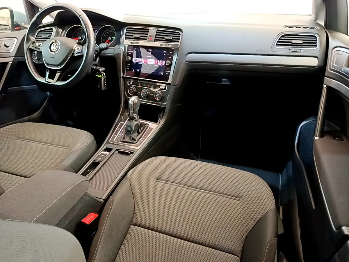 Intérieur de Volkswagen Golf 2019 vu côté passager, tableau de bord noir avec écran tactile et sièges tissu gris.
