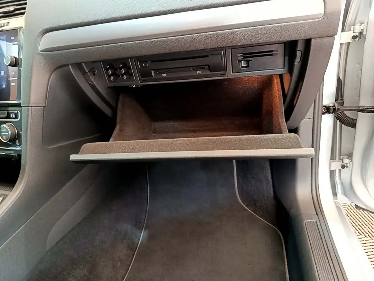 Gros plan sur la boîte à gants ouverte côté passager d'une Volkswagen Golf gris clair 2019, intérieur noir.