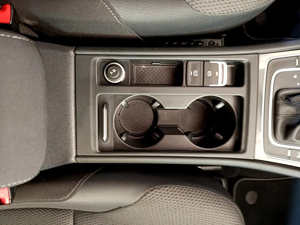 Vue plongeante sur la console centrale noire avec porte-gobelets et bouton frein à main électrique d'une Volkswagen Golf gris clair 2019
