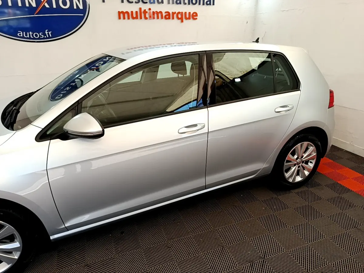 Profil côté gauche d'une Volkswagen Golf gris clair 2019 garée en intérieur sur sol damier noir et rouge