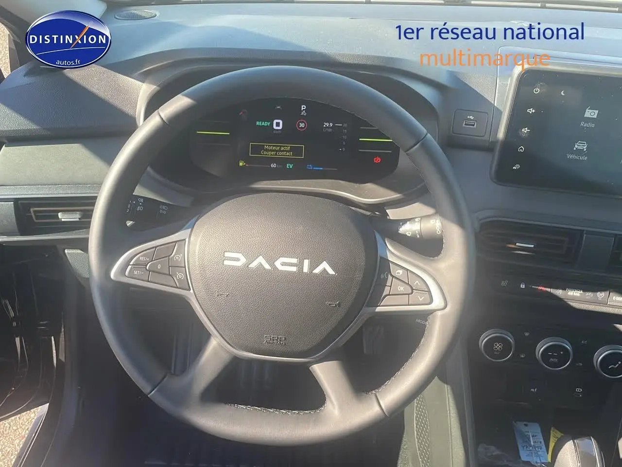 Vue intérieure centrée sur le volant DACIA noir avec tableau de bord digital et écran tactile à droite.