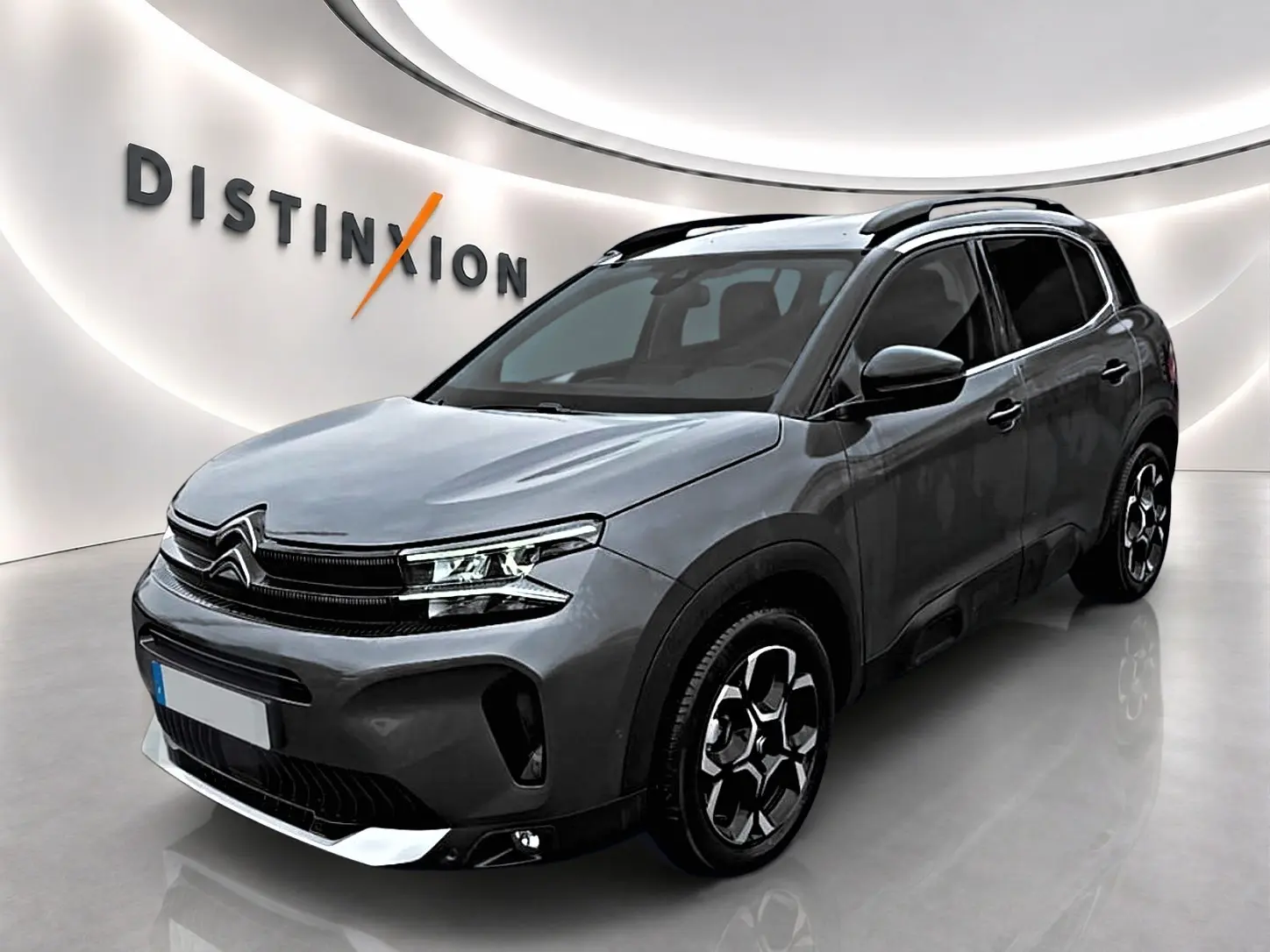 Citroën C5 Aircross gris vue 3/4 avant droit avec barres de toit et jantes alu distinctives.