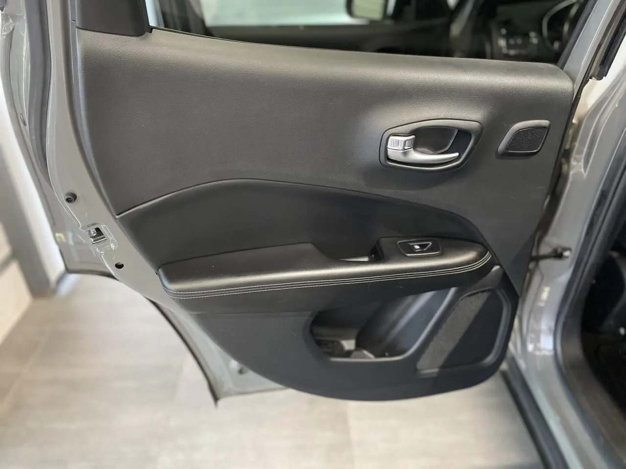 Porte arrière droite ouverte du Jeep Compass gris foncé, montrant la garniture intérieure noire avec commande de vitre.
