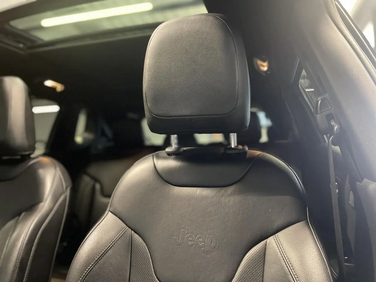 Gros plan sur le siège avant en cuir noir embossé Jeep, avec toit ouvrant panoramique visible en arrière-plan.