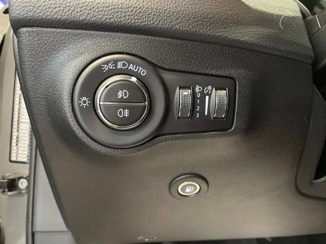 Gros plan sur les commandes d'éclairage et l'ouverture de trappe à carburant du tableau de bord noir d'un Jeep Compass Trailhawk.