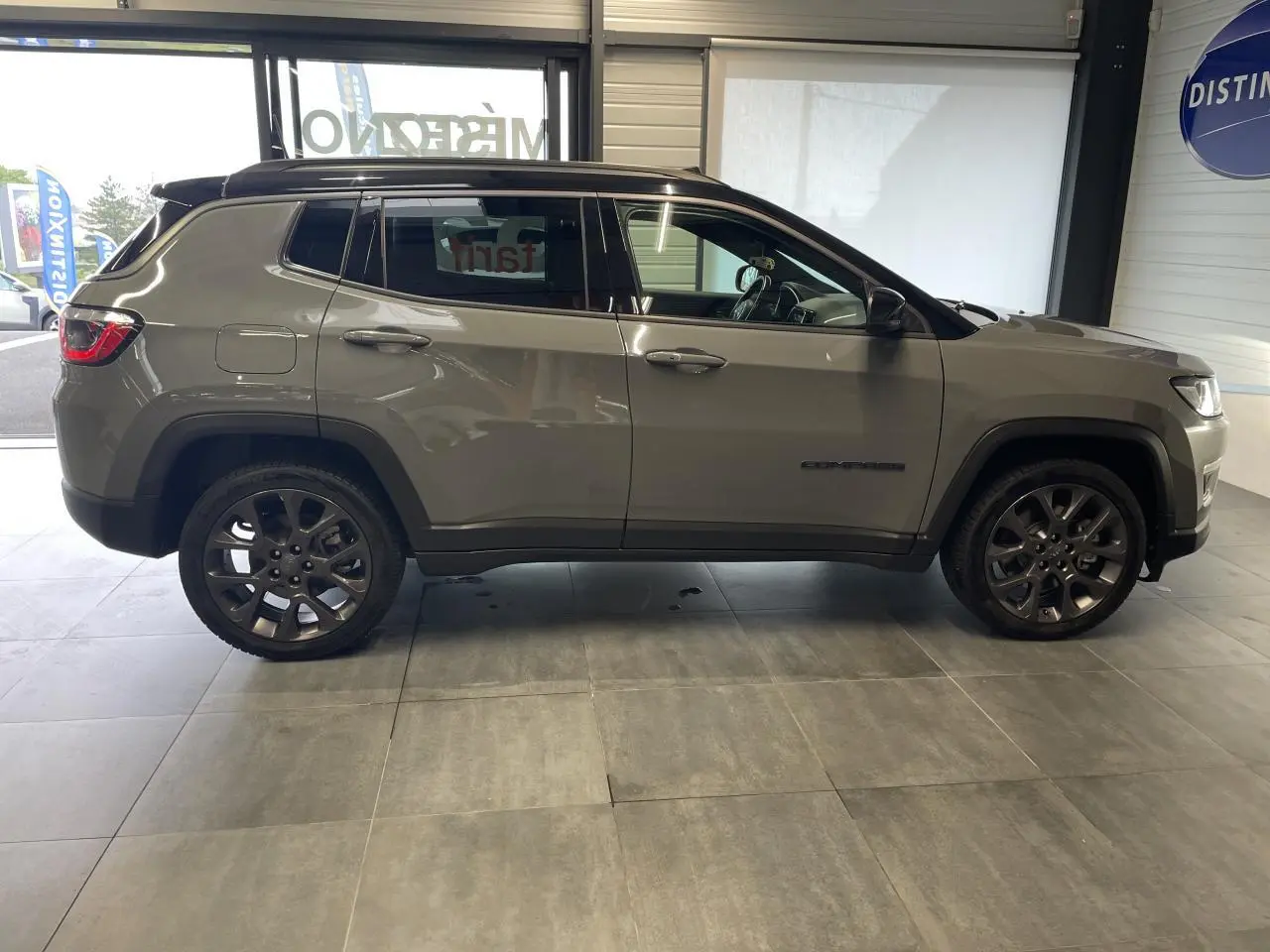 Profil côté gauche d'un Jeep Compass gris foncé avec jantes alliage et toit noir en intérieur showroom.