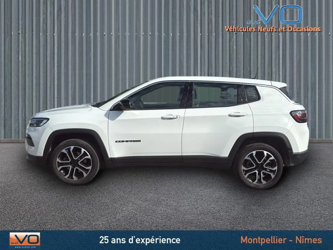 Profil côté gauche du Jeep Compass blanc 2024 avec jantes alliage 18 pouces sur fond industriel.