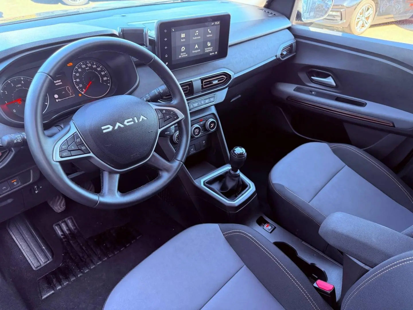 Vue intérieure côté conducteur de la Dacia Sandero 2025, volant multifonction, écran tactile et sièges tissu brun cuivré.