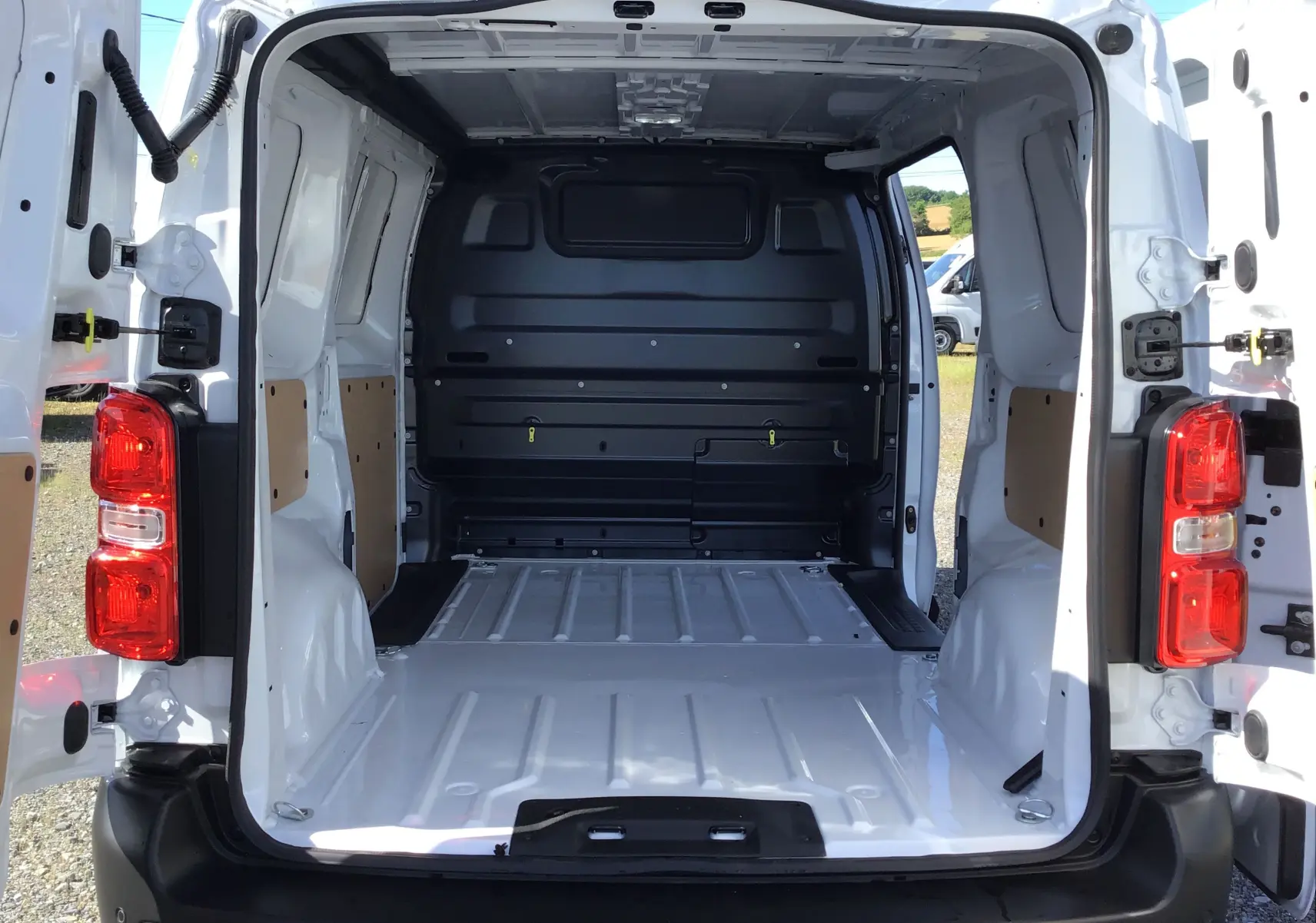 Vue arrière ouverte du fourgon blanc Peugeot Expert M 1.5 BlueHDi 120, montrant l'espace de chargement vide et les portes battantes.