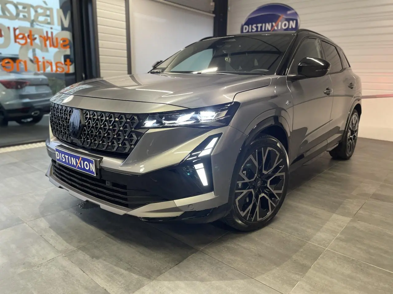 Renault Austral gris métallisé en 3/4 avant droit, avec calandre noire et jantes alliage 20 pouces distinctives.