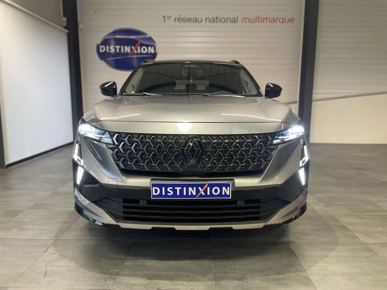 Vue frontale d'un Renault Austral gris métallisé avec calandre noire et feux LED allumés en intérieur showroom.
