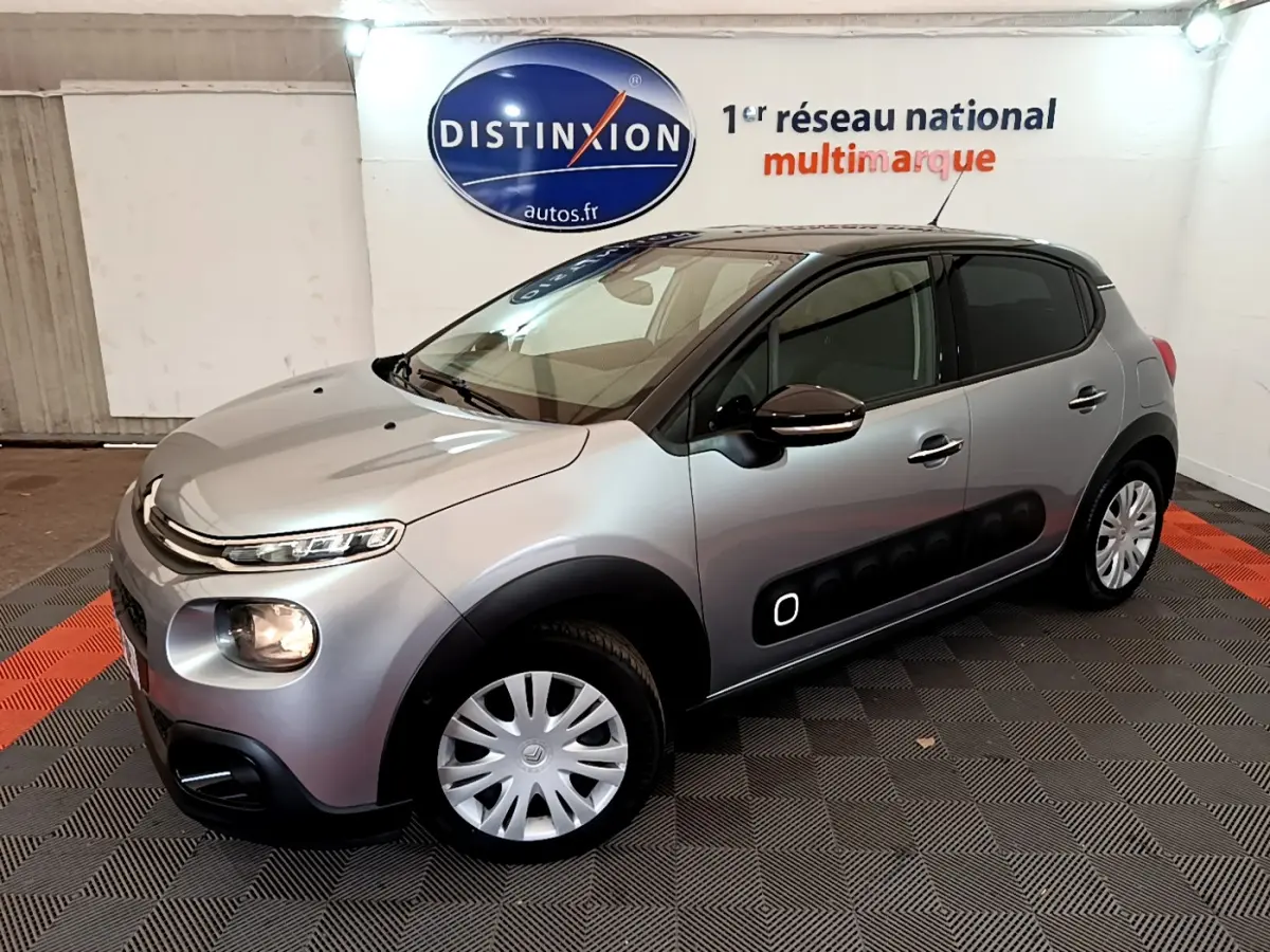 Citroën C3 gris clair vue 3/4 avant droit, avec protections latérales noires et jantes acier à enjoliveurs.