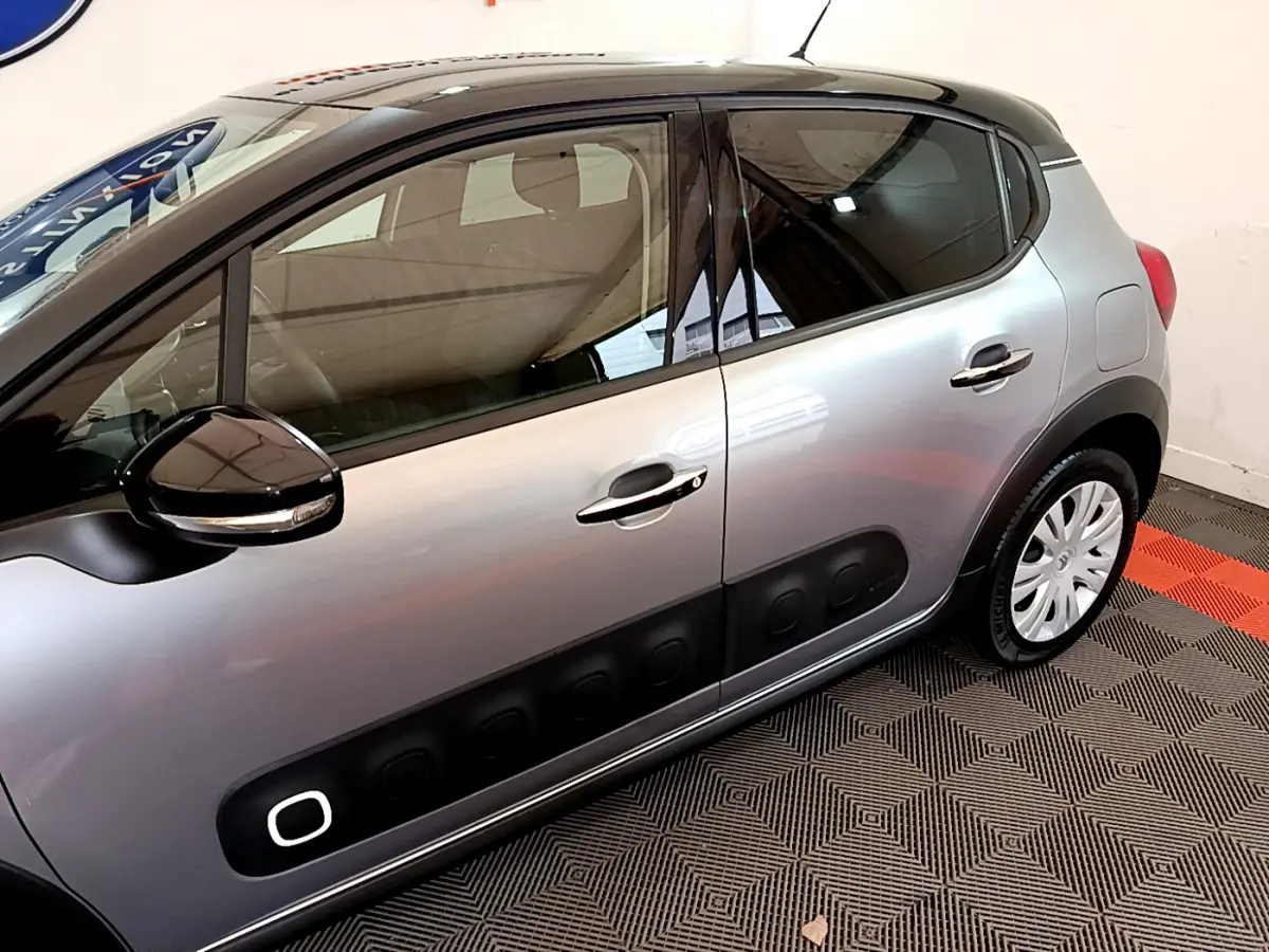 Vue latérale côté gauche d'une Citroën C3 gris clair avec protections noires caractéristiques sur les portières.