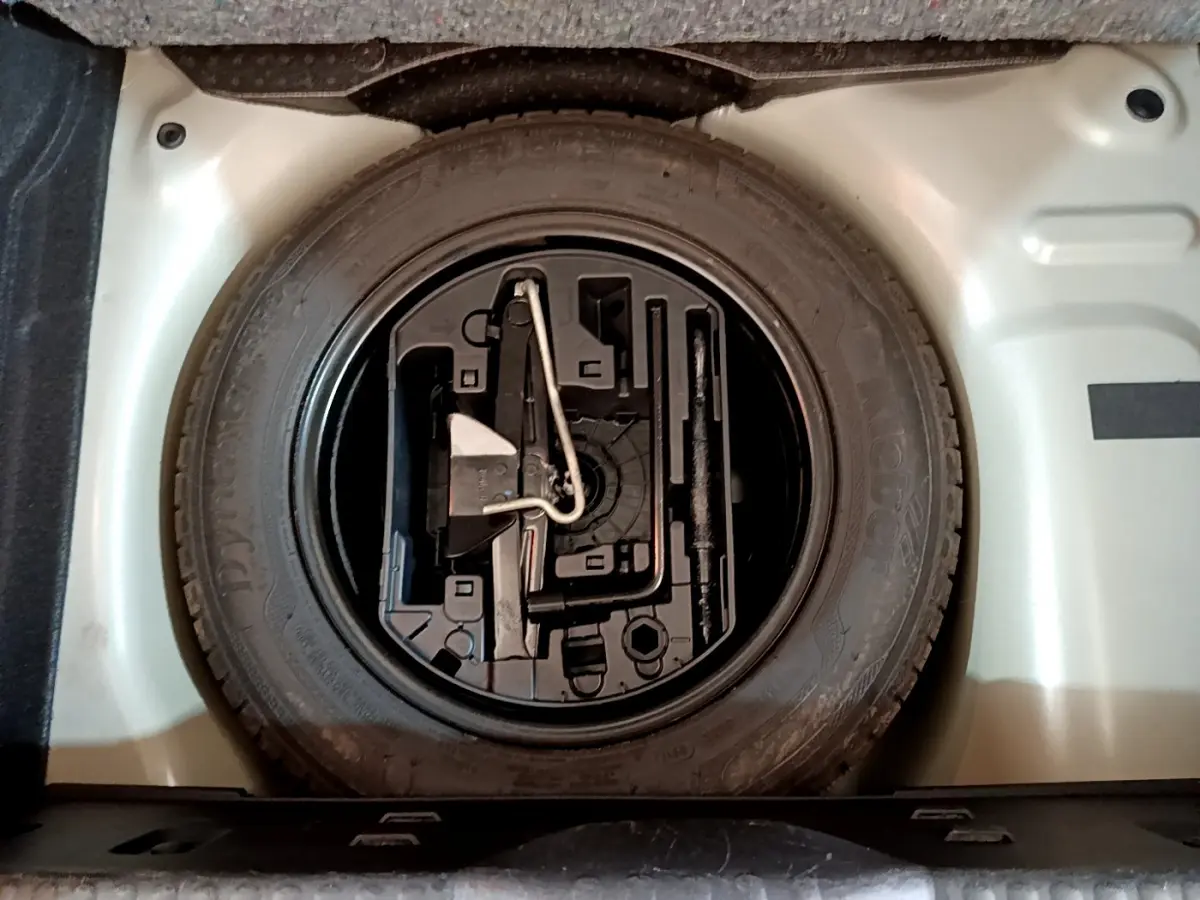 Gros plan sur la roue de secours et son rangement dans le coffre gris clair d'une Citroën C3 2019 PureTech Shine Business.