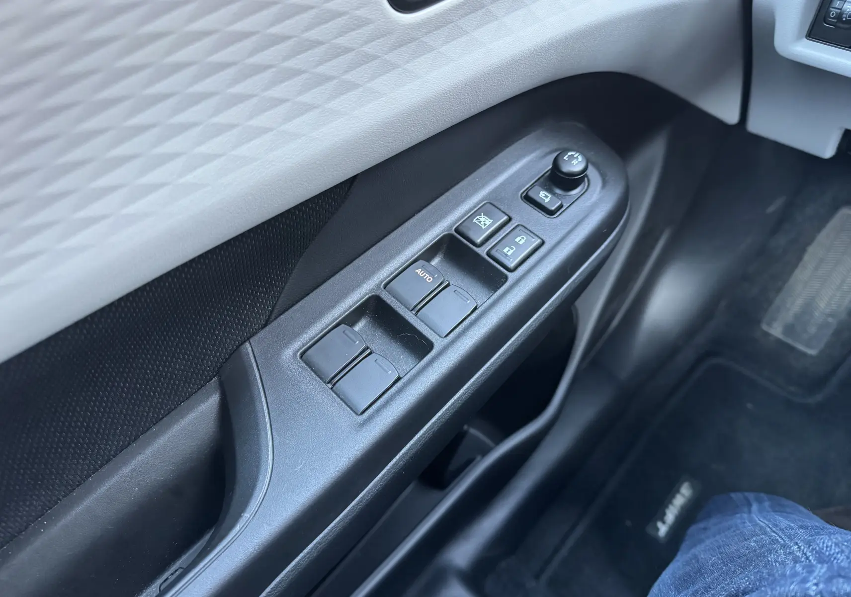 Gros plan sur la commande des vitres et rétroviseurs côté gauche de la porte intérieure d'une Suzuki Swift 2024 blanc/gris.