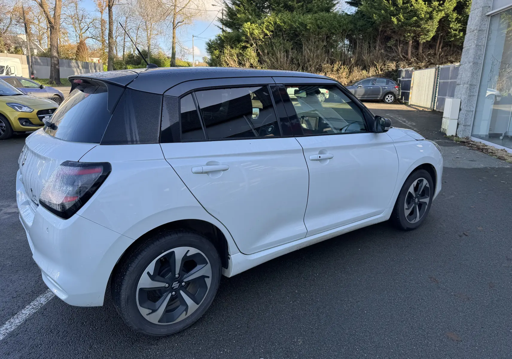Suzuki Swift 1.2 Dualjet Pack Auto Hybrid blanc et gris vue 3/4 arrière côté droit, toit noir contrasté.