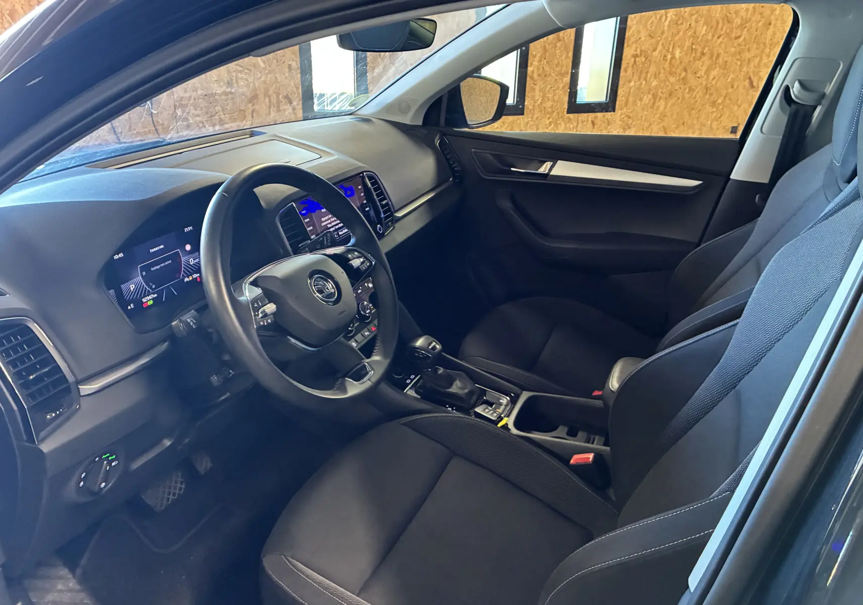 Intérieur avant droit du Skoda Karoq noir 2024, volant multifonctions, tableau de bord digital et sièges tissu noirs.