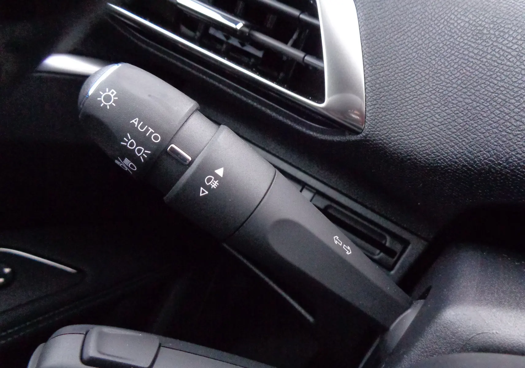 Gros plan sur la commande des feux et clignotants à gauche du volant dans l'habitacle noir du Peugeot 3008 bleu Celebes 2023.