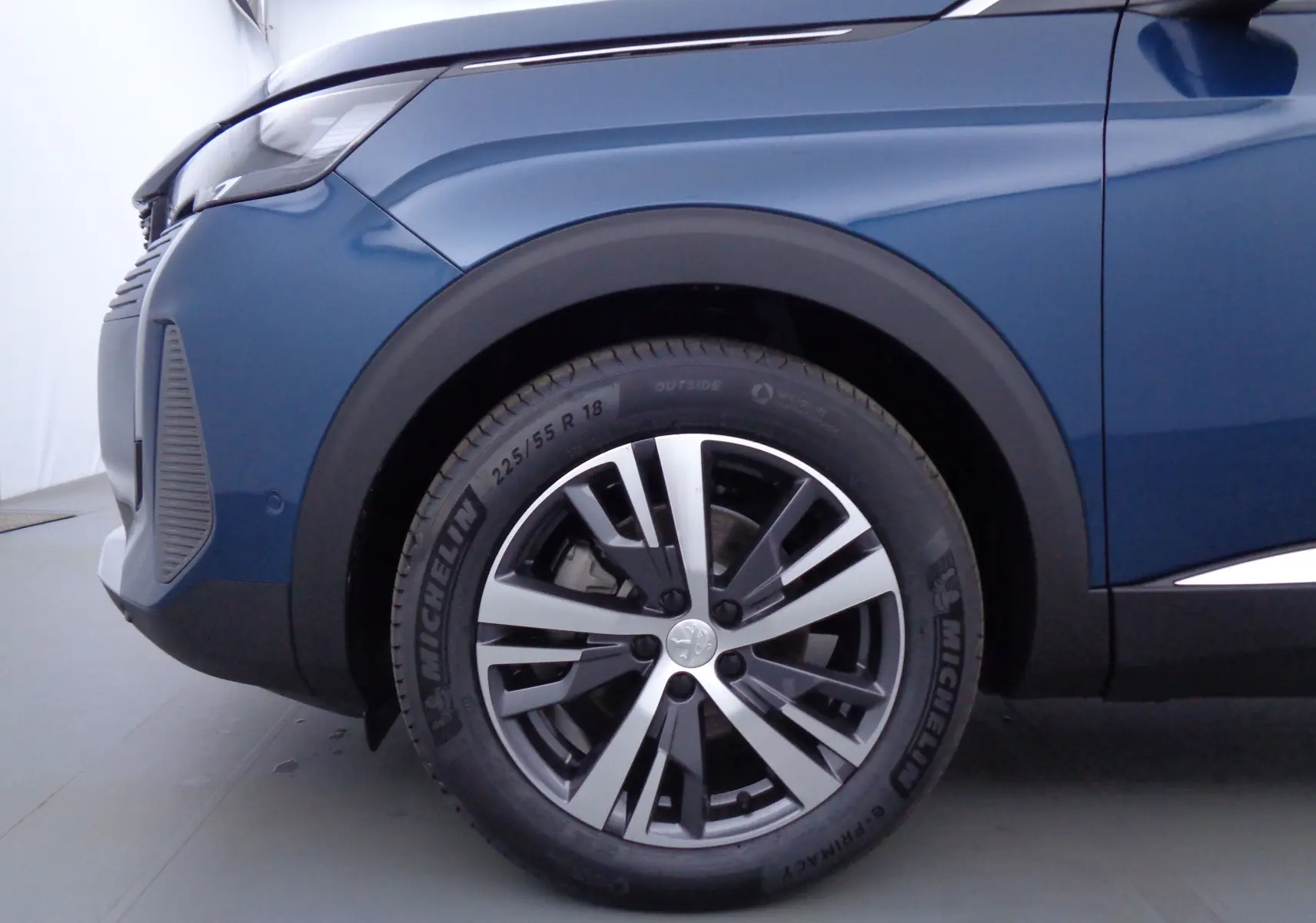 Gros plan sur la roue avant gauche d'un Peugeot 3008 bleu Célèbes Métal avec jante alliage et pneu Michelin.