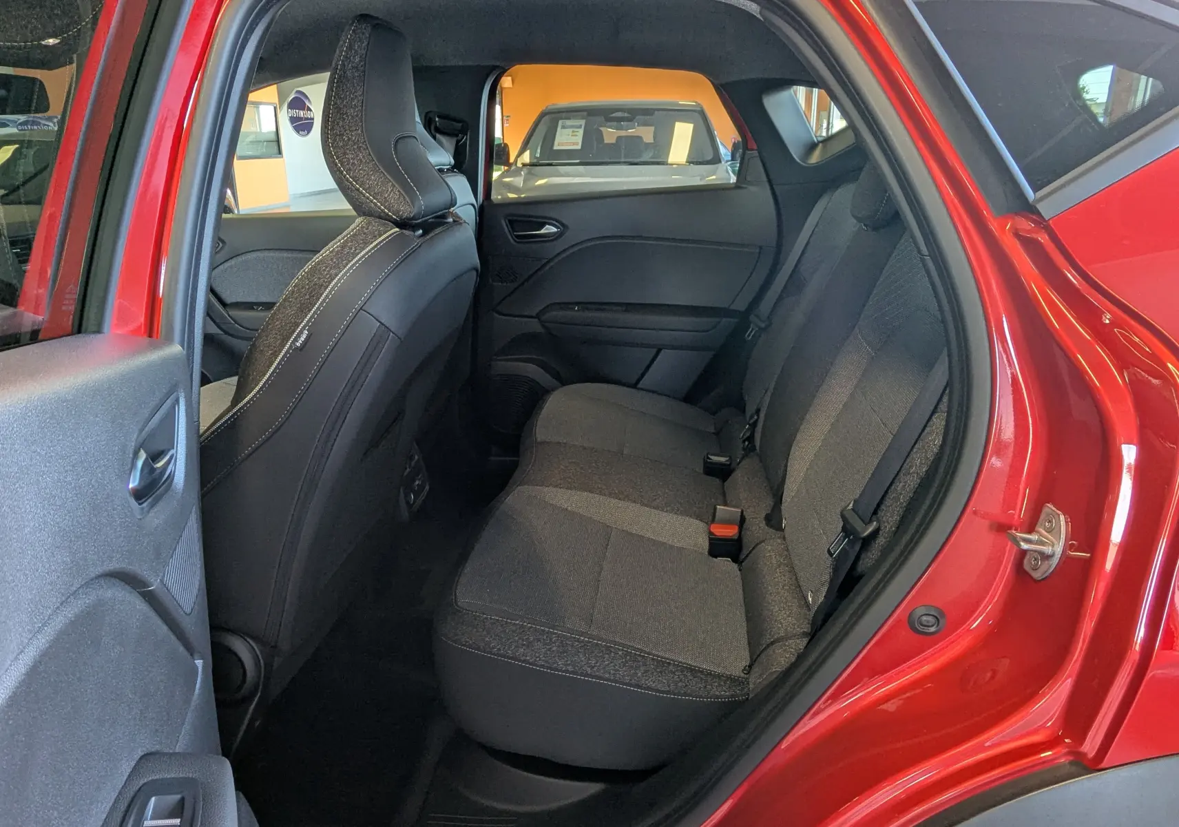 Vue intérieure arrière côté droit du Renault Captur 2025 rouge flamme, montrant les sièges arrière en tissu gris.