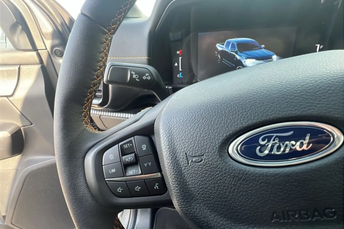 Vue rapprochée du volant cuir noir avec surpiqûres orange et tableau de bord digital du Ford Ranger gris carbone 2025.