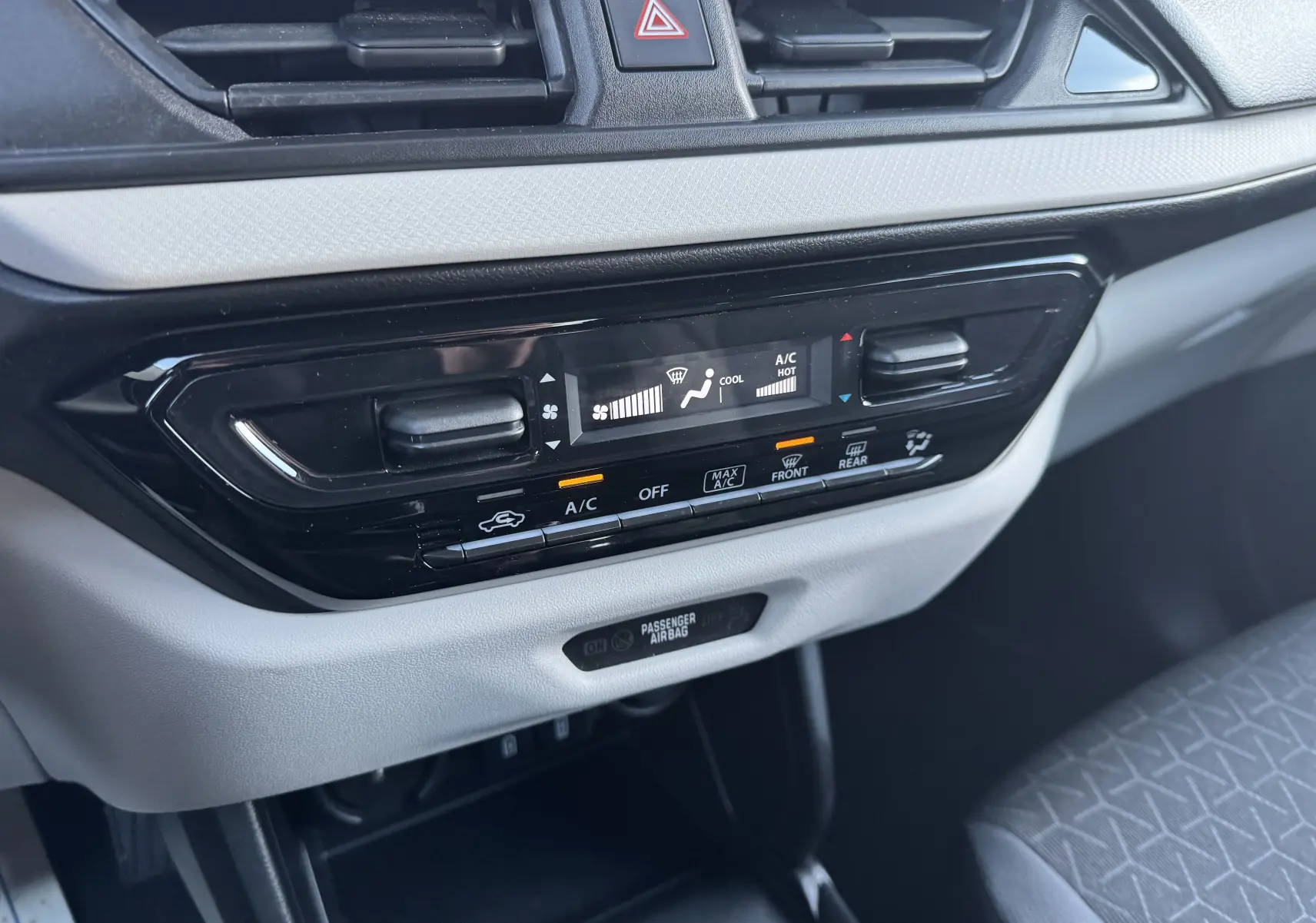 Gros plan sur la console centrale de la Suzuki Swift blanche 2025, montrant les commandes de climatisation et l'airbag passager.