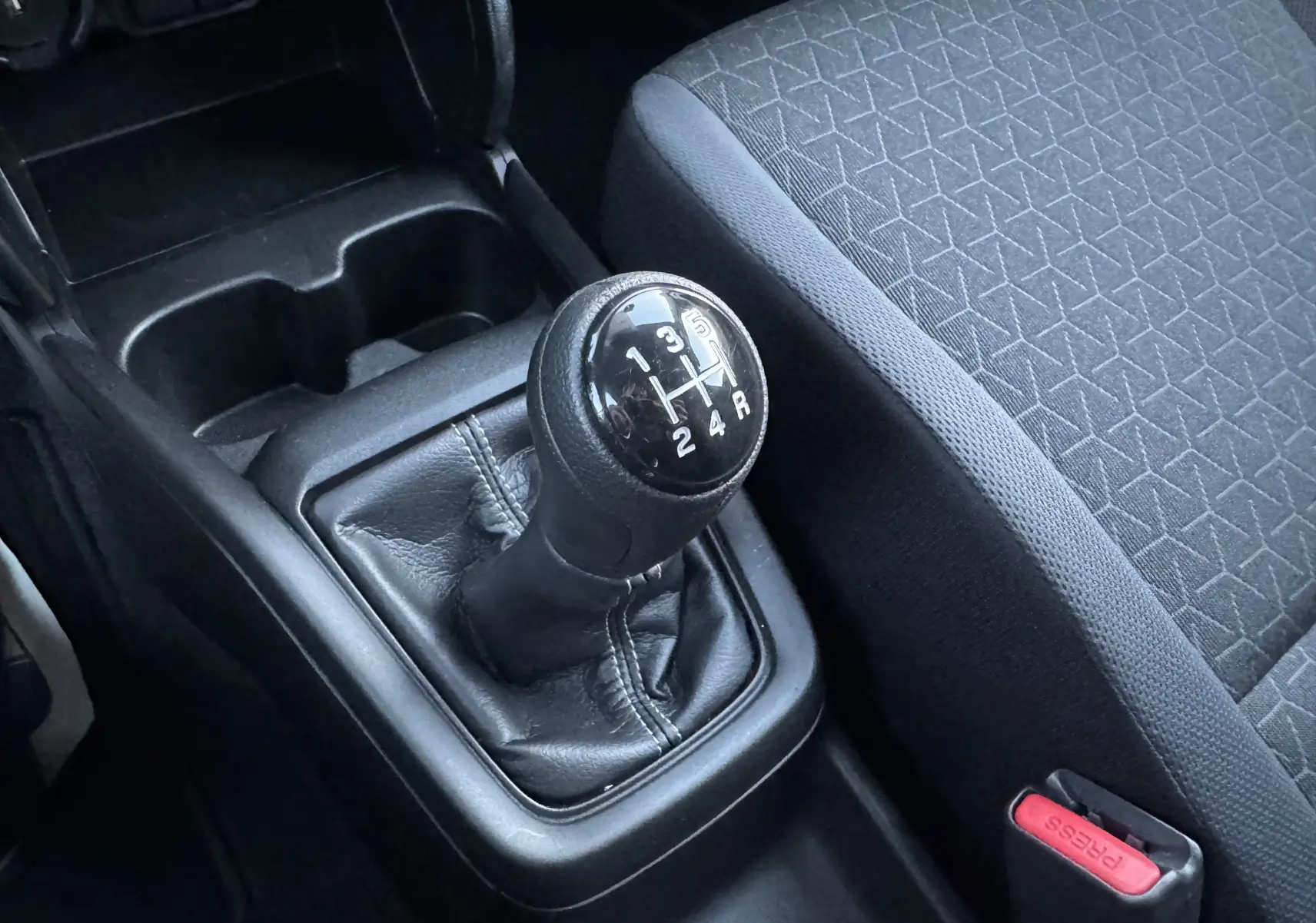 Gros plan sur le levier de vitesses manuel noir et le siège tissu gris à motifs géométriques dans une Suzuki Swift blanche 2025.