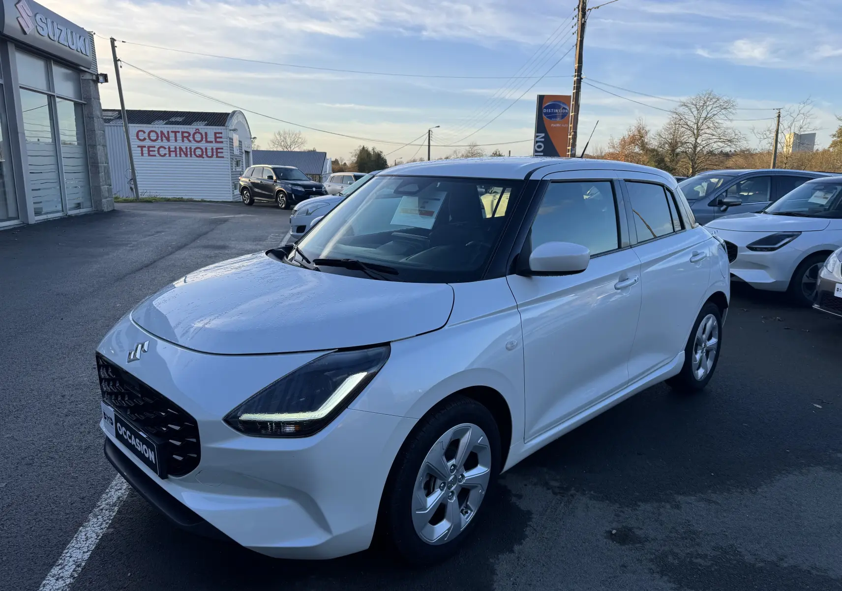 Suzuki Swift 1.2 Privilège Hybrid blanc vue 3/4 avant droit, avec calandre noire et feux LED en forme de C.
