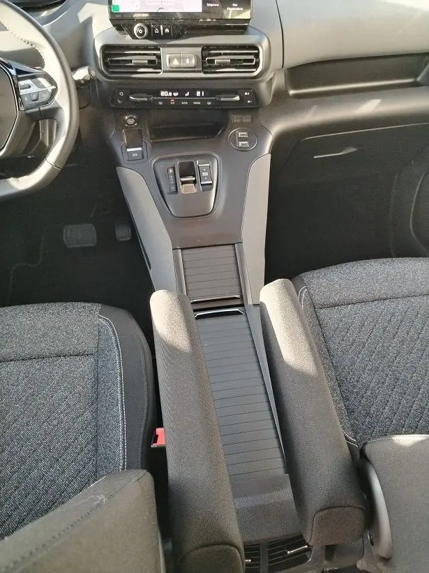 Vue intérieure centrée sur la console centrale et levier de vitesse du Peugeot Rifter 2025, sièges gris foncé visibles.