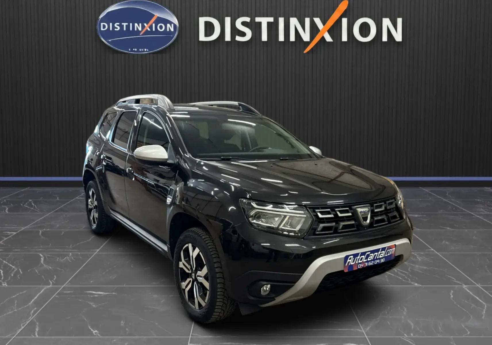 Dacia Duster noir en 3/4 avant droit, avec rétroviseurs blancs et jantes bi-ton, sur fond intérieur showroom.