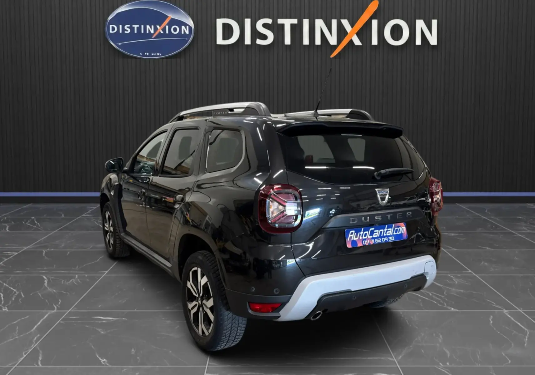 Vue 3/4 arrière droite d'un Dacia Duster noir 2022 avec jantes bi-ton et barres de toit visibles en intérieur showroom.