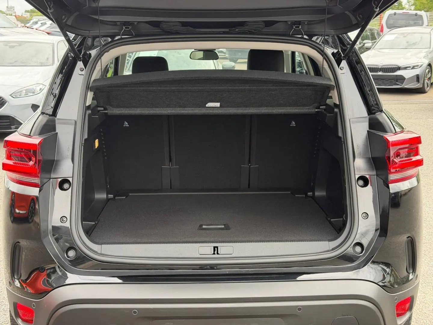 Coffre ouvert vu de l’arrière d’un Citroën C5 Aircross noir Perla Nera avec cache-bagages et feux arrière LED visibles.