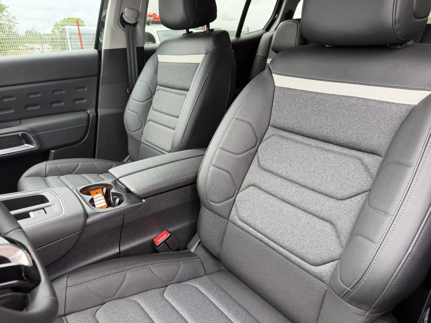 Vue rapprochée des sièges avant gris tissu et cuir du Citroën C5 Aircross 2025, avec accoudoir central et console.