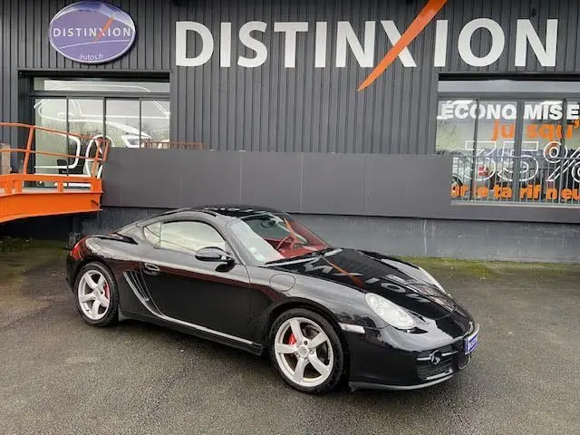 Porsche Cayman noir vue 3/4 avant droit, jantes argentées et étriers de frein rouges, stationnée devant un bâtiment.
