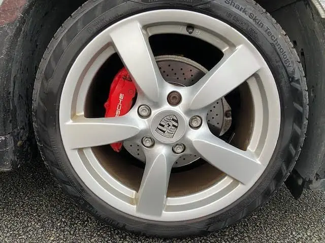 Gros plan sur la jante argentée de Porsche Cayman 2008 avec étrier de frein rouge marqué Porsche visible derrière.
