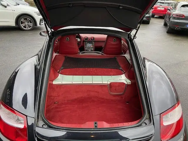 Vue arrière du coffre ouvert d'une Porsche Cayman noire de 2008, intérieur rouge avec sièges sport visibles.