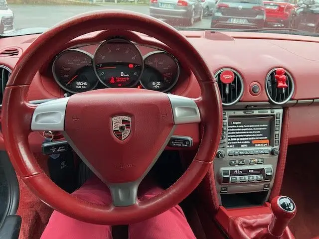 Intérieur rouge d'une Porsche Cayman 2008, vue du conducteur sur tableau de bord et levier de vitesse manuel.