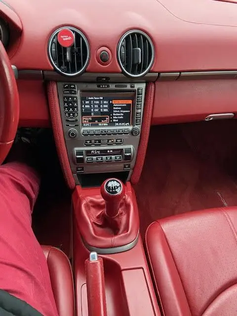 Intérieur rouge vif du Porsche Cayman 2.7L 2008, vue centrée sur la console avec levier de vitesse manuel et tableau de bord numérique.