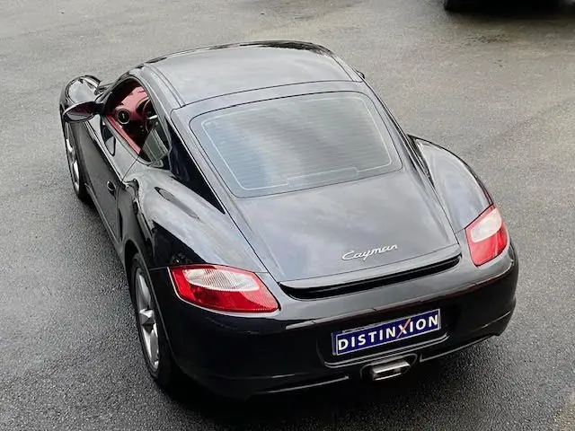 Vue 3/4 arrière d'une Porsche Cayman noire 2008 avec intérieur rouge visible et plaque Distinxion.