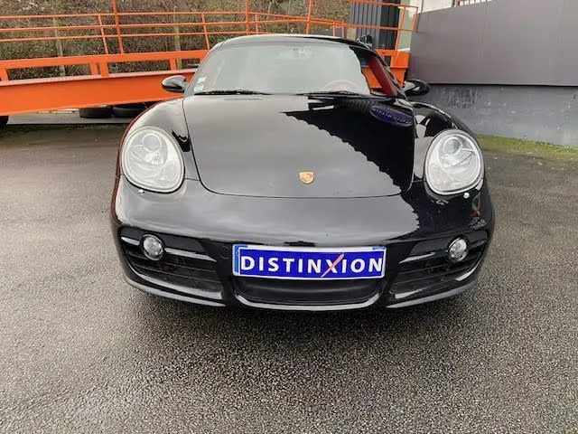 Vue de face d'une Porsche Cayman noire de 2008 avec plaque Distinxion sur un sol asphalté.